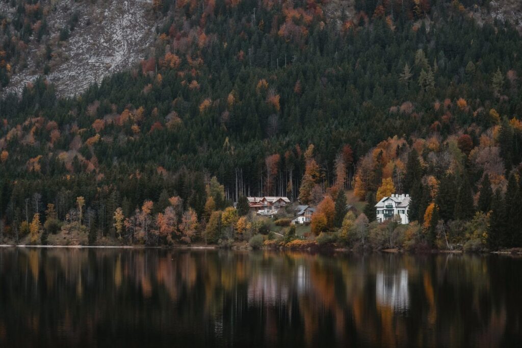 A chalet and a villa on a wooded shore, reflected in the lake
